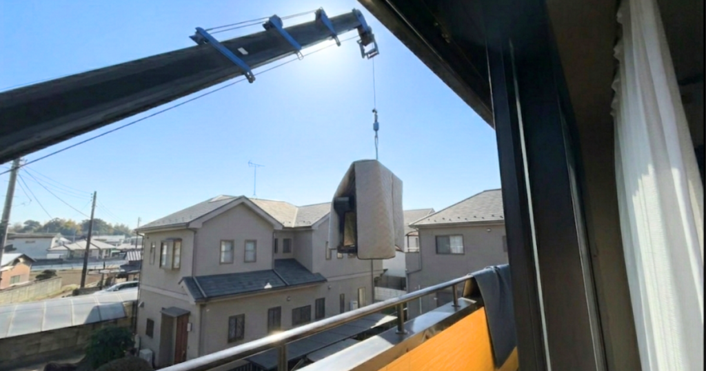 クレーン車の長く伸びたアームの先にロープ1本でぶら下がってるいるピアノ