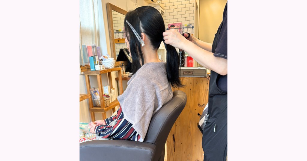 結婚式当日の朝、美容室で前開きの服を着て着付け前のヘアセットを受けている様子